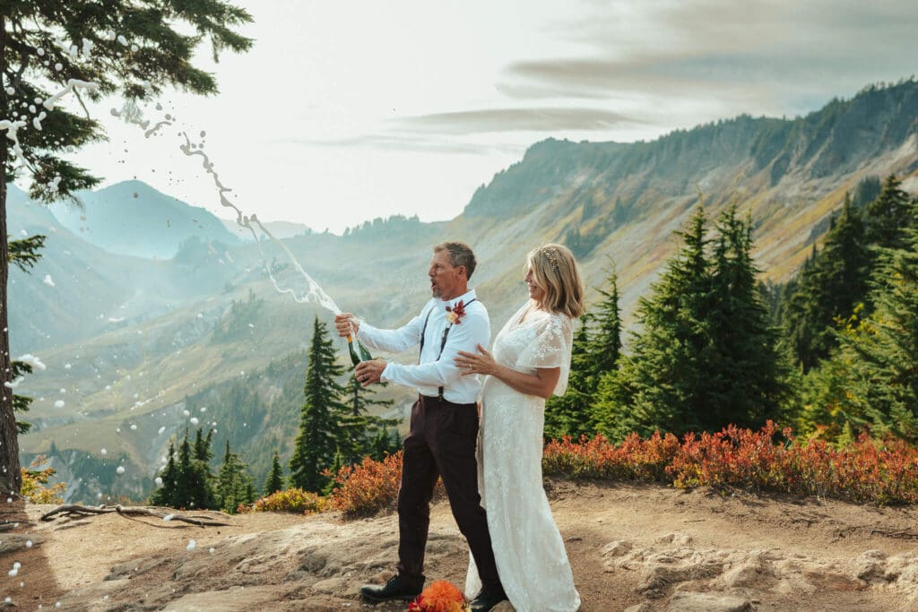 Couple celebrating their elopement at Artist Point with a champagne pop and Mount Baker views in the background.