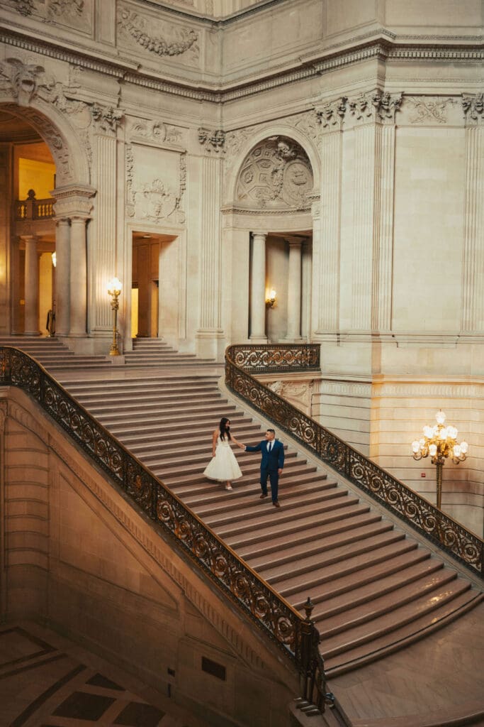 Wide cinematic photo of a couple holding hands on the staircase at San Francisco City Hall