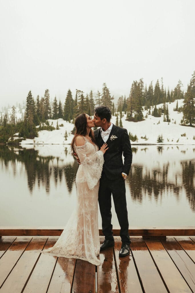 A moody wedding portrait of a couple sharing a quiet kiss by a snowy lake Picture Lake in My Baker National Forest, photographed by a Snohomish wedding photographer.