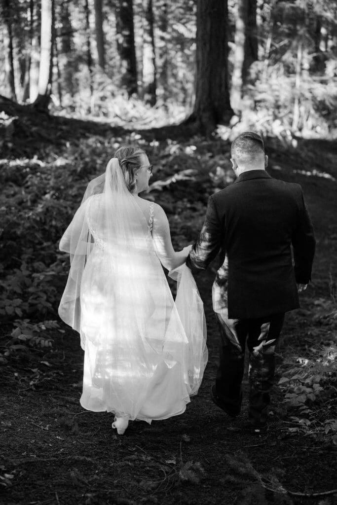 Black and white photo of a wedding couple walking hand-in-hand through the forest near Floral Hall in Everett, WA.