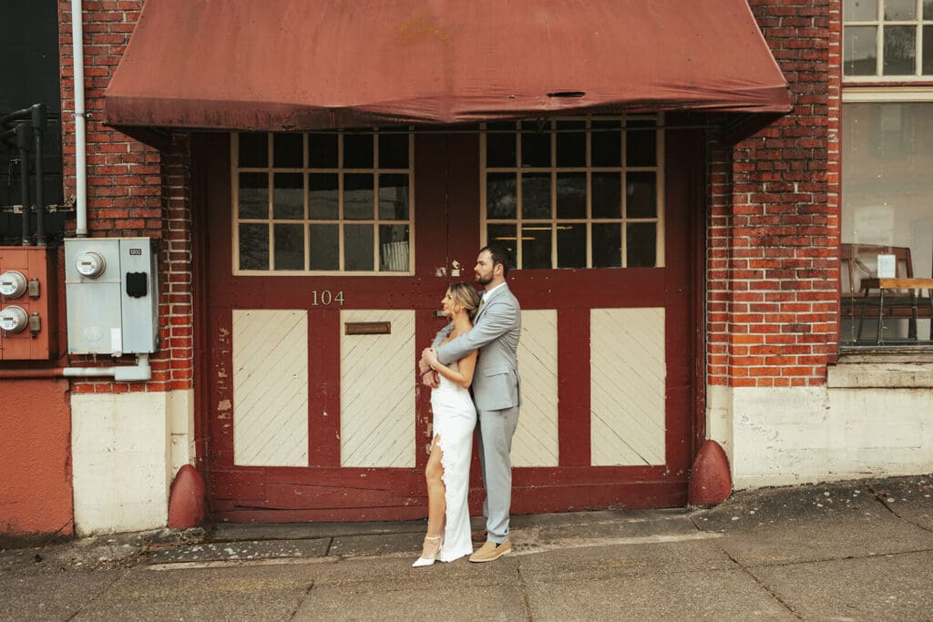 The couple stands together in front of a large red garage door on a brick building in downtown Snohomish.