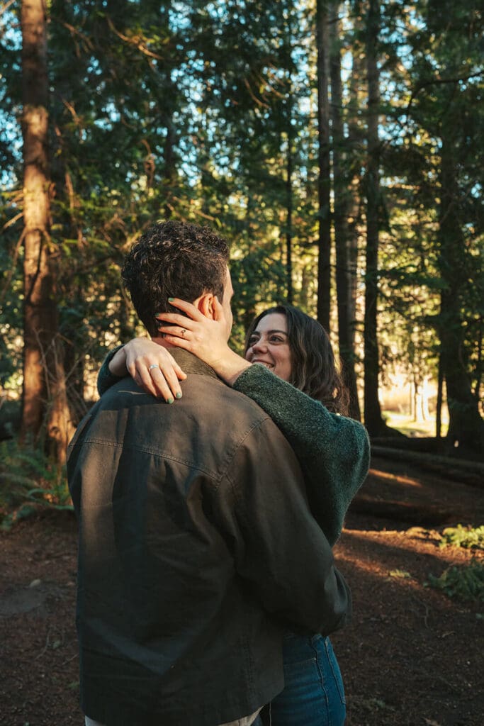 Close-up candid engagement photo with warm sunlight in the trees at Flowing Lake County Park near Snohomish, WA.