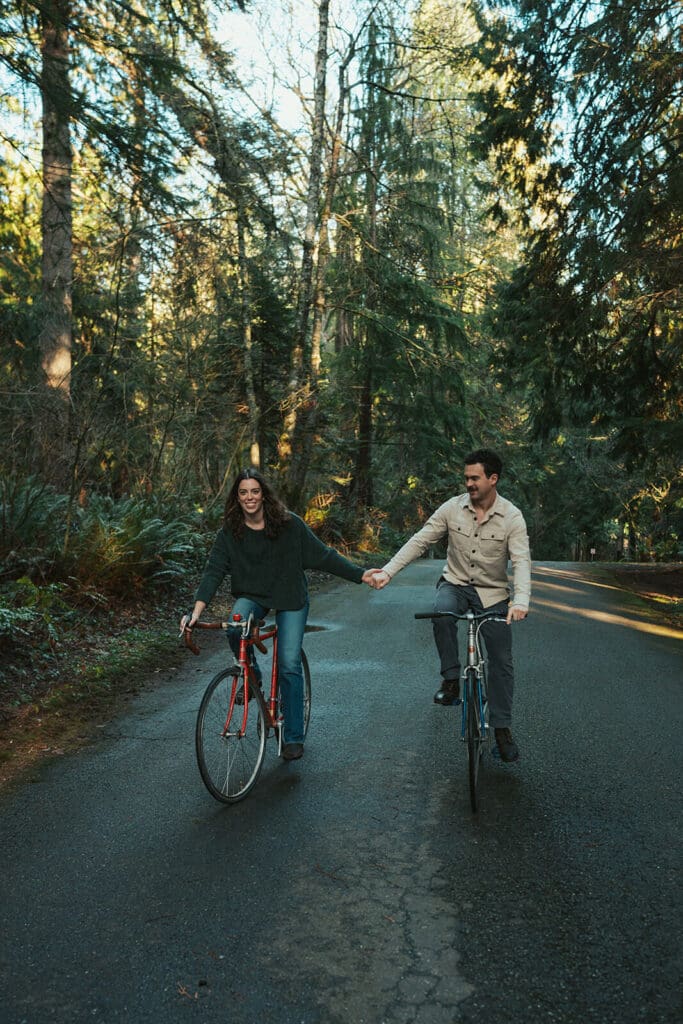 Cinematic engagement photos riding bikes on a quiet forest road at Flowing Lake County Park in Snohomish County, Washington.