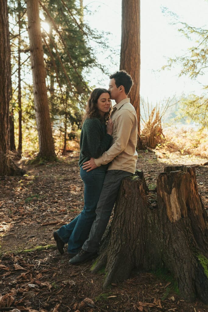 Romantic cinematic engagement photo in a pine forest with warm backlight at Flowing Lake County Park near Snohomish, Washington.