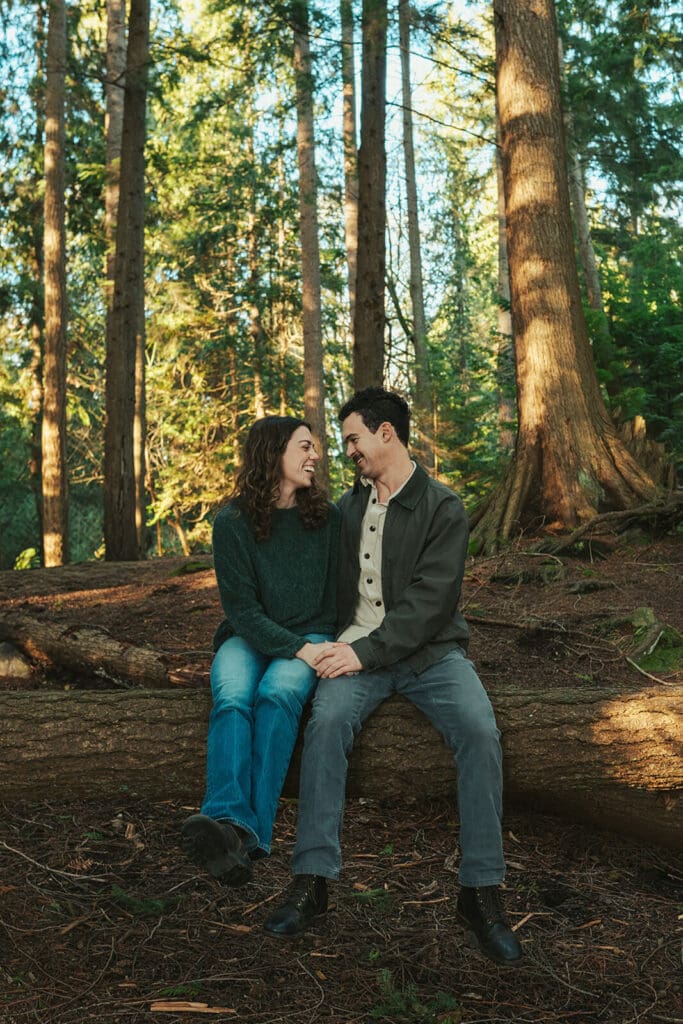 Vintage-inspired engagement portraits on a fallen log in an evergreen forest at Flowing Lake County Park in Snohomish County.