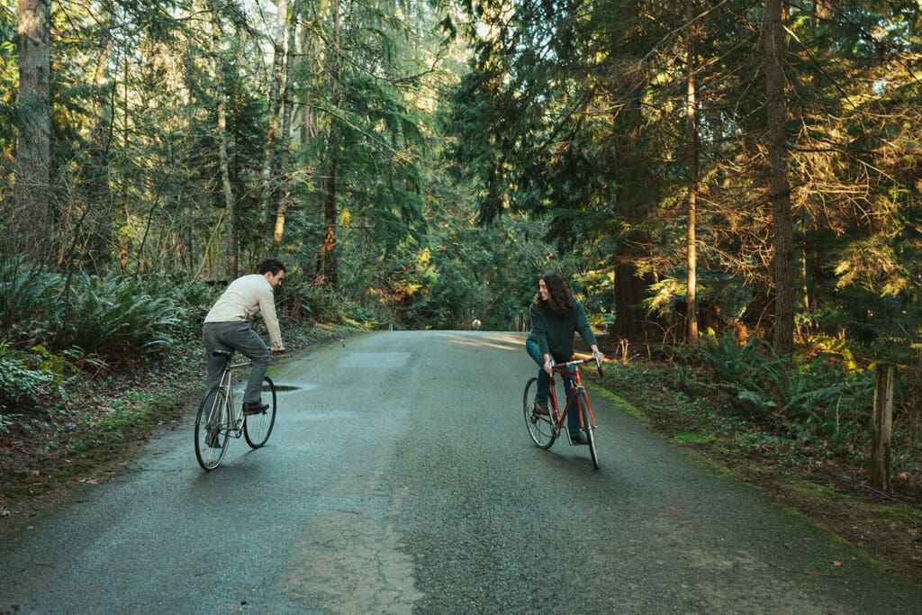 Wide cinematic engagement photo on a forest road surrounded by evergreens at Flowing Lake County Park in Snohomish County.