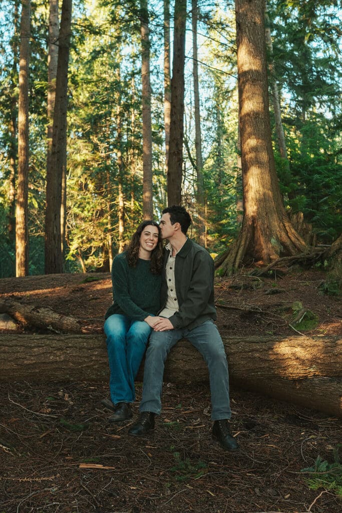 Romantic forest engagement photo with soft golden light and tall evergreens at Flowing Lake County Park near Snohomish, WA.