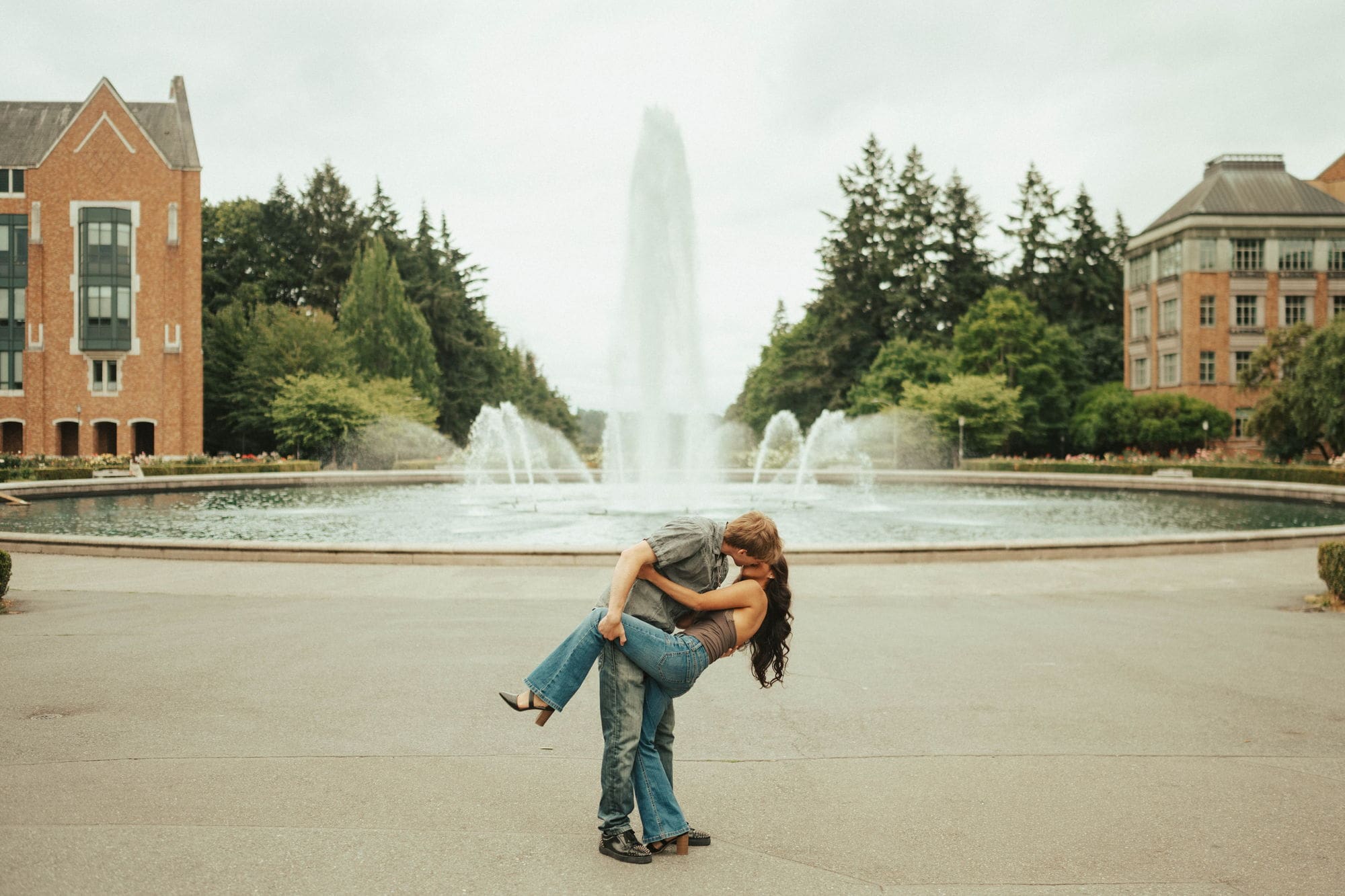 Man dipping his partner for a kiss in front of a tall fountain on the University of Washington campus