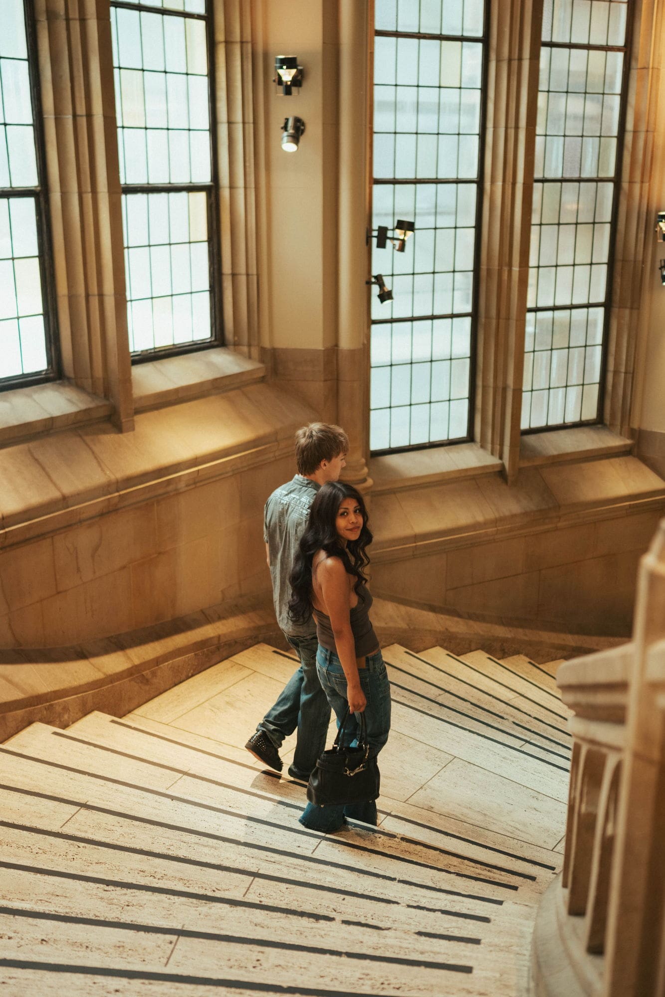 Woman glancing back over her shoulder as the couple walks down a sunlit stone staircase landing