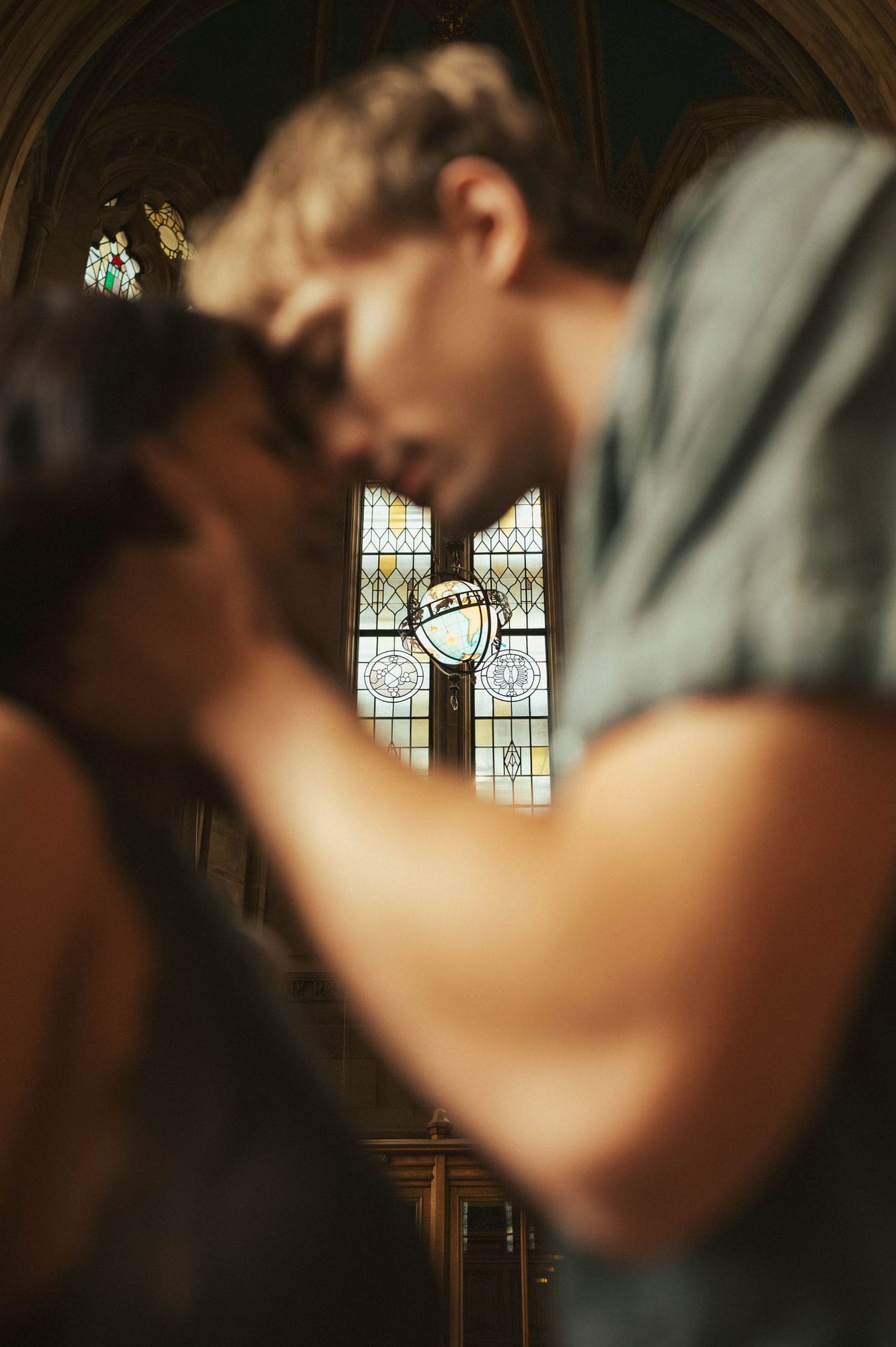 Blurred couple in the foreground with a stained glass window and hanging globe in sharp focus behind them
